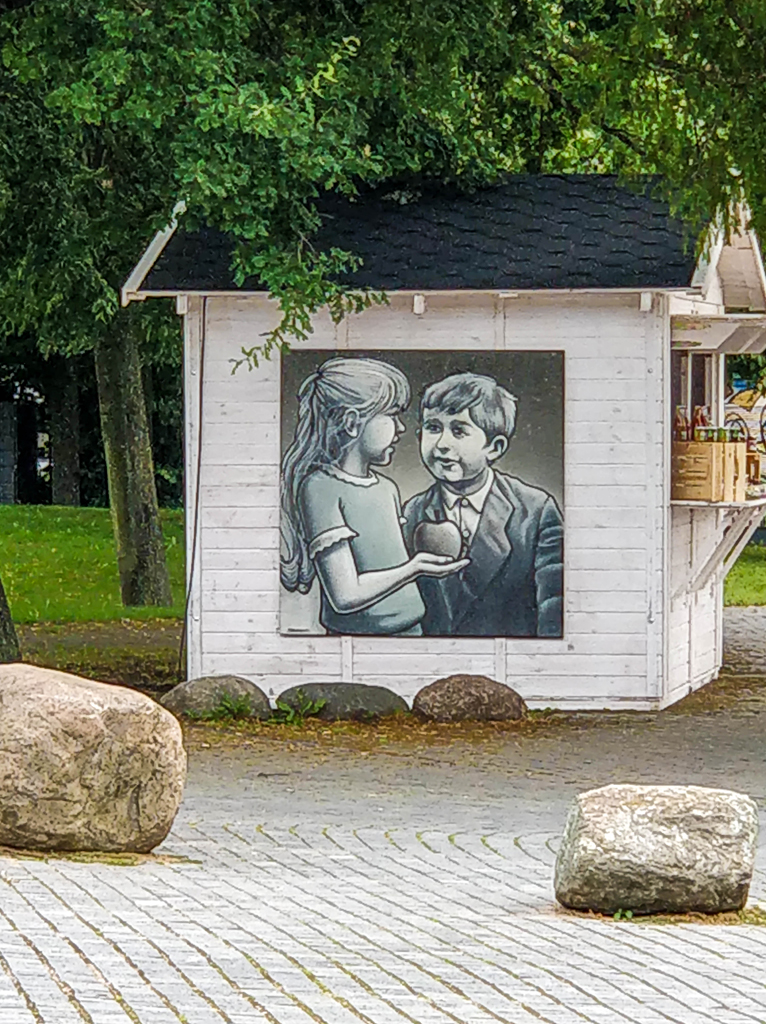 Holzkiosk in weiß mit Graffity zweier Kinder in Grautönen. Das Mädchen hält einen Apfel in der Hand