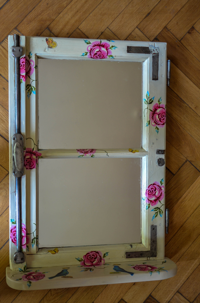 altes Fenster mit Holzablage mit Spiegelfläche und rosa Rosen auf beigem Holz versehen