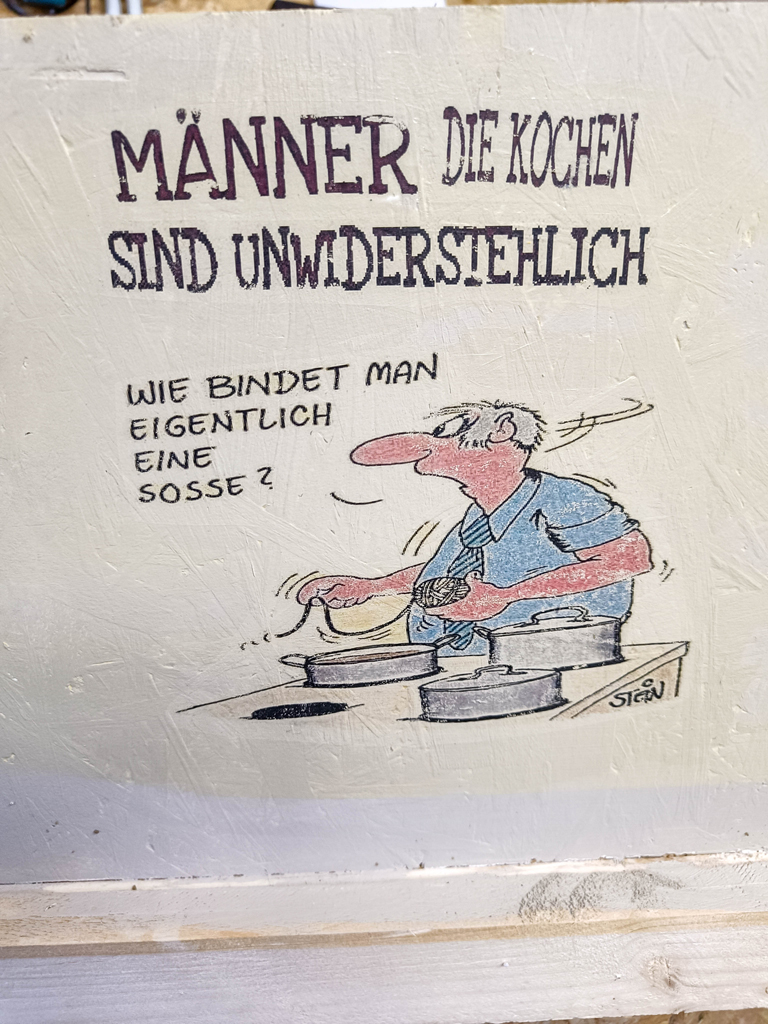 Comic Uli Stein: Männer die kochen sind unwiderstehlich. Darunter steht: Wie bindet man eigentlich eine Soße? Ein Mann mit Wollfaden am Herd abgebildet.