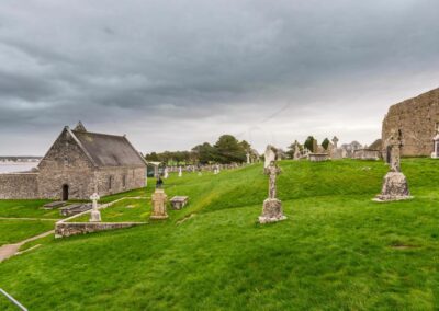 Wiese mit antiken Kreuzen auf maigrüner Wiese an der Klosterruine Clonmacnoise. Links ist der Shannonfluss zu sehen