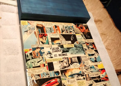 alte Holzkiste in dunkelblau gestrichen und mit Comics von Alain Landier beklebt