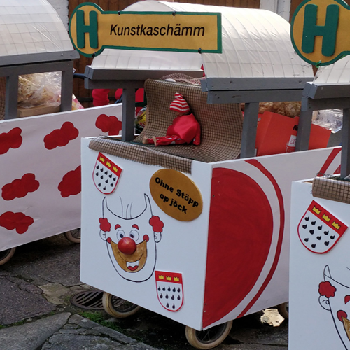 Karnevalswagen in rot weiß mit Kunstkaschämm Haltestelle und Clown mit Köln-Wappen vorne drauf