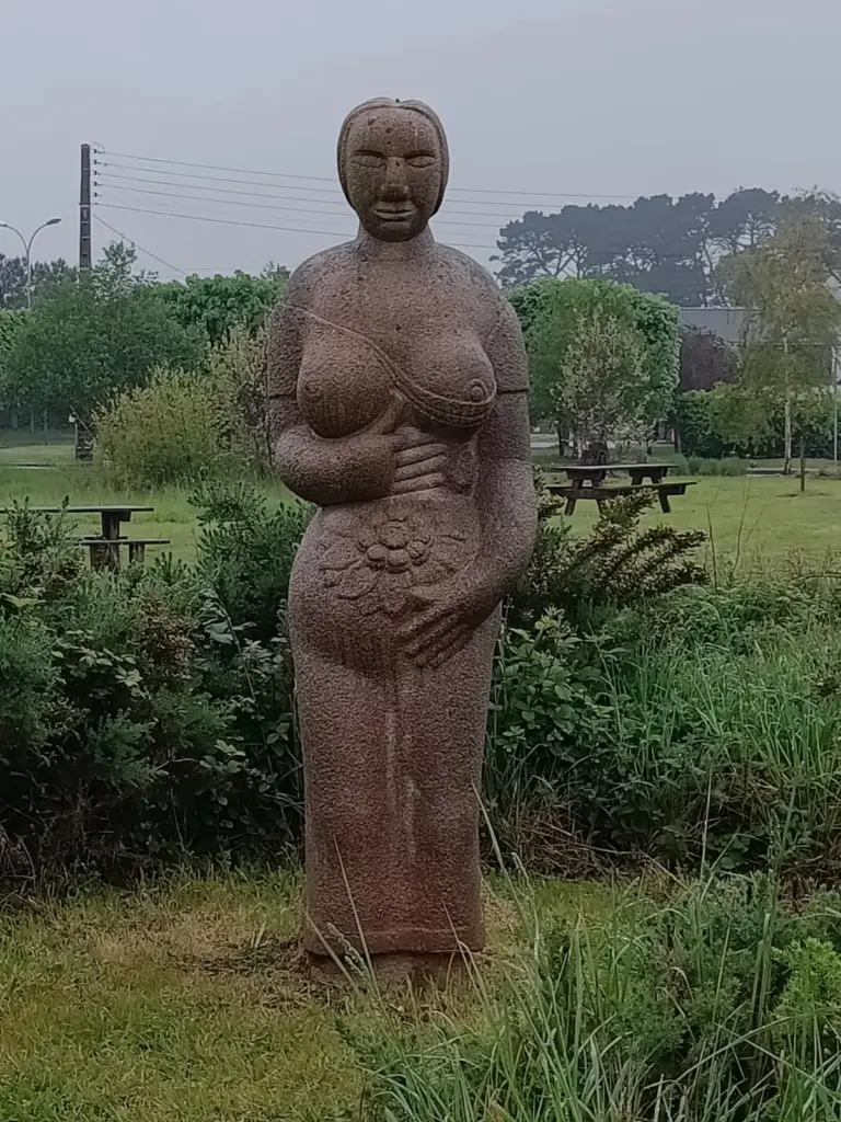 riesige Frauenskulptur mit nackten Brüsten, die sich mit den Händen den Bauch hält und dort eine Blüte eingemeißelt hat. Skulpturenpark in Ploumanach