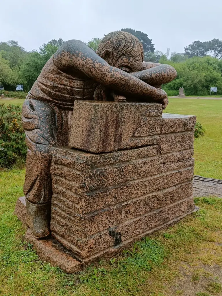 Skulptur aus Granit mit Mann der mit dem Kopf auf seinen Armen auf einem Quader liegt im Park von Ploumanach