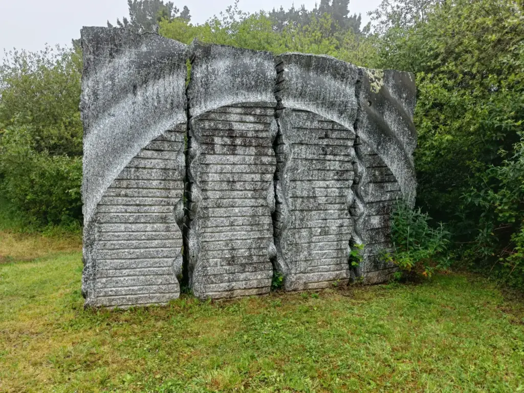 Vorderseite von Schieferskulptur, die den Lauf des Wassers darstellen soll. Vier rechteckige Säulen mit ein wenig Abstand und Rillen eingemeißelt. Darüber sieht es wie ein Torbogen aus.