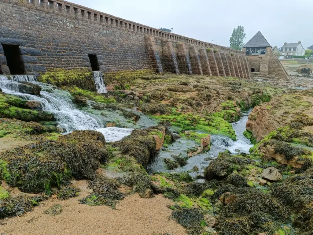 Wasserdurchlauf durch alte Mauer zwischen zwei Prielen mit alter Mühle bei Ebbe in Tourony