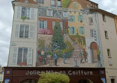 großen buntes Wandbild was eine Häuserfassade mit einem Platz davor darstellt