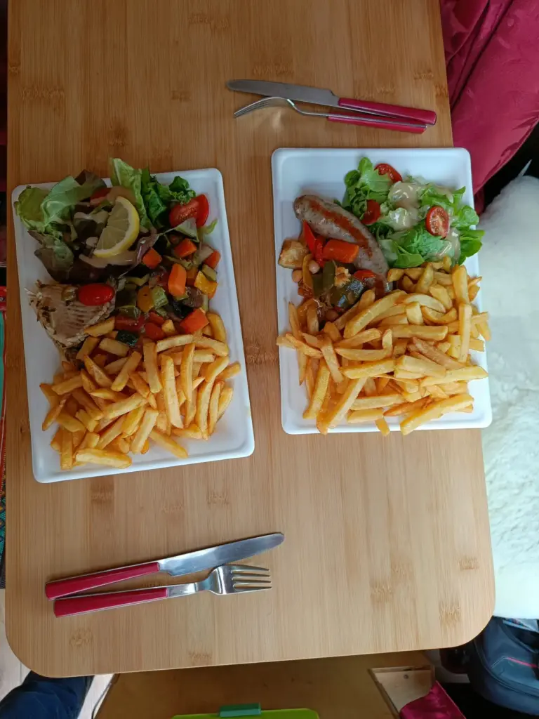 Im Campingbus Essen vom Foodtruck auf rechteckigen Tellern, einmal Wurst und einmal Rochen mit Fritten und Salat