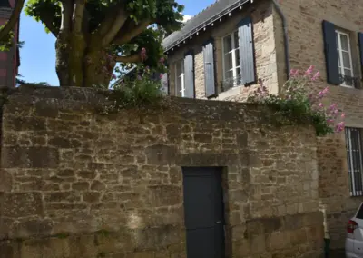 alte Mauer mit Haus und gestutzten Bäumen, dahinter liegt eine Villa