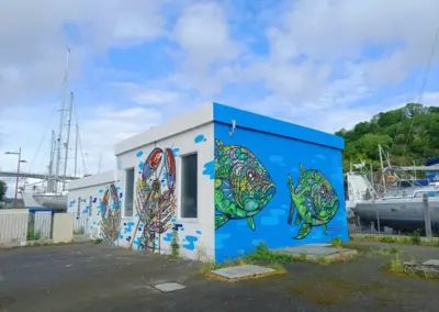 Graffitis Hafen von Légué, Bretagne. Gebäudecontainer mit zwei Fischen in buntem grün auf blauem Hintergrund und daneben zwei bunten Krabben