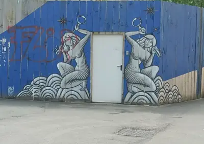 Graffity auf Bauzaun mit zwei nackten Frauen die einen Schlüssel hinter dem Kopf halten. Hintergrund blaue Farbe und Frauen in schwarz mit Grautönen